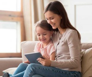 Happy Mom and Kid Daughter Using Digital Tablet Sitting on Sofa